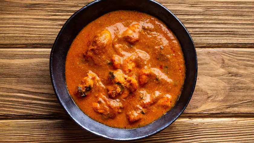 Top view of Indian chicken curry in rich tomato gravy on a rustic wooden background, traditional butter chicken tikka masala suitable for ready-to-eat retort meal packaging.