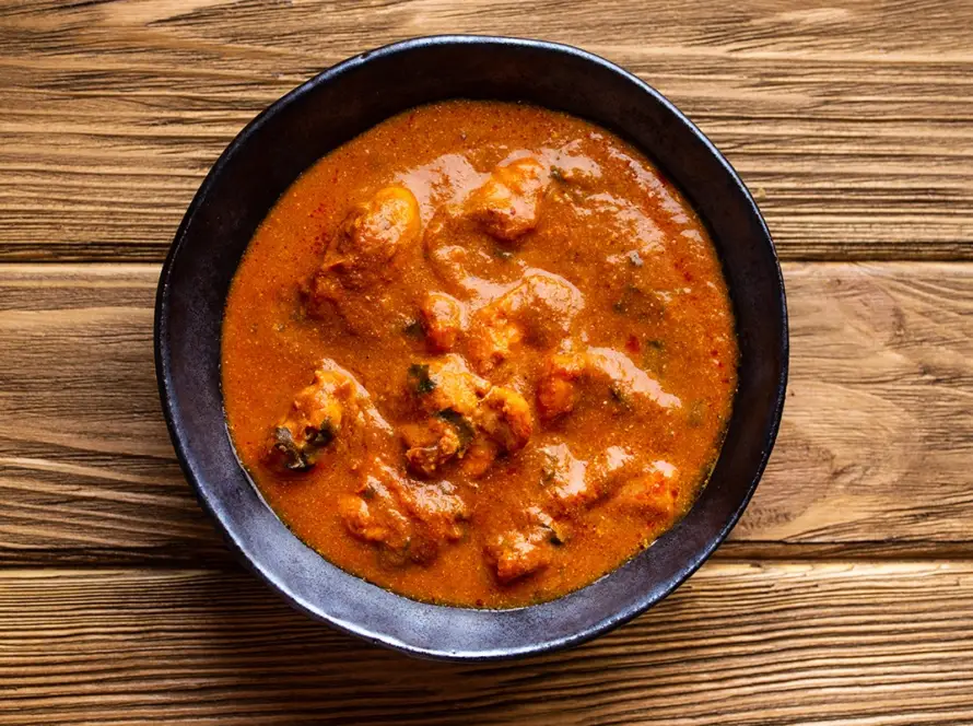 Top view of Indian chicken curry in rich tomato gravy on a rustic wooden background, traditional butter chicken tikka masala suitable for ready-to-eat retort meal packaging.