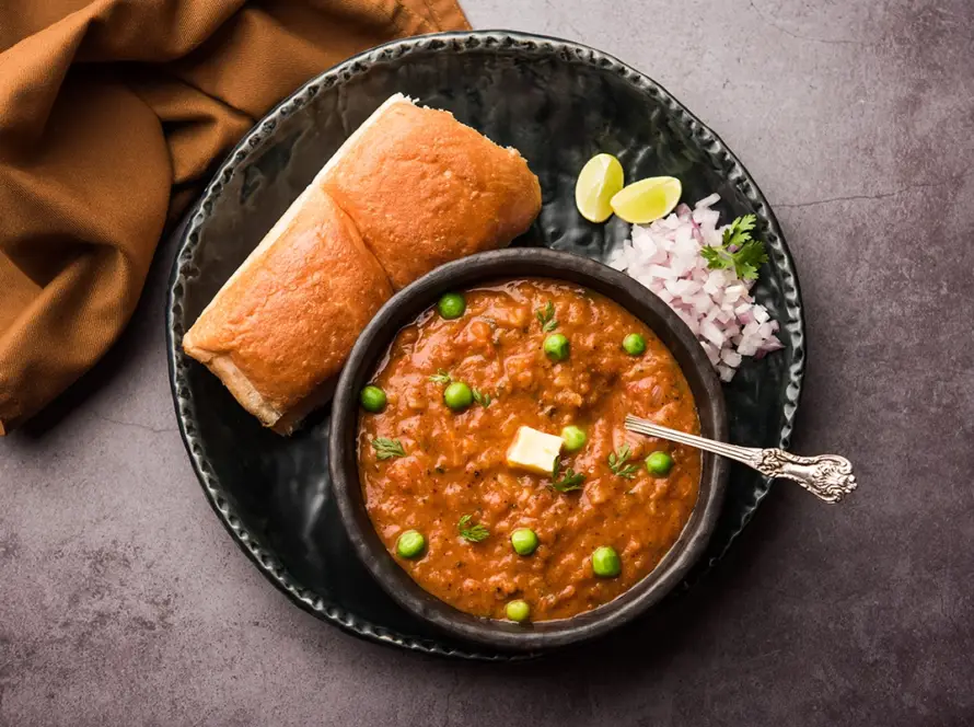 Top view of authentic Mumbai style Pav Bhaji served on a partition plate with buttered pav buns, chopped onions, and a lemon wedge.