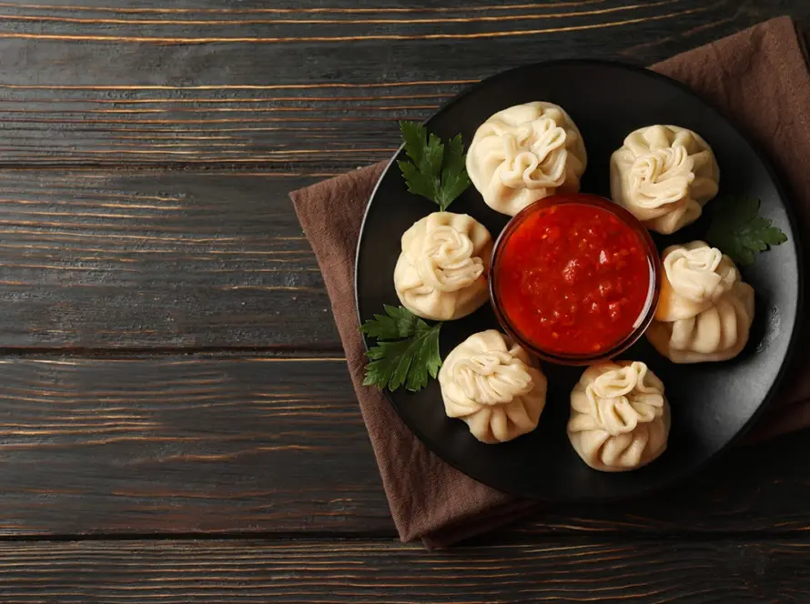 Top down view of steamed Tibetan momos arranged in a circle with a center bowl of spicy red garlic sauce for B2B kiosk supply.