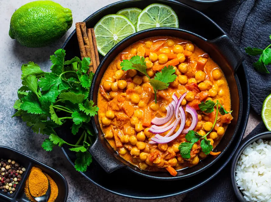 Top view of vegan chickpea curry (Chole) served with basmati rice and fresh cilantro in a black bowl against a dark background, showcasing the Golden Grain legume module.