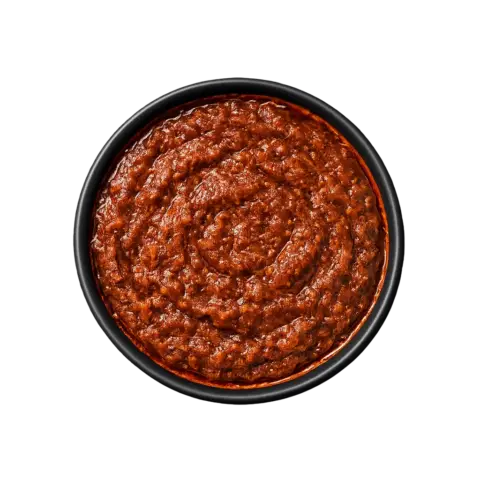 A professional 90-degree top-down flat lay of Pot and Ladle brand Andhra Nellore Biryani Paste. The concentrated masala is a deep, dark reddish-brown with a thick, textured consistency. Visible flecks of crushed spices, peppercorns, and a glossy oil sheen indicate a slow-roasted base. Served in a small, minimal black china bowl on a seamless white studio background.