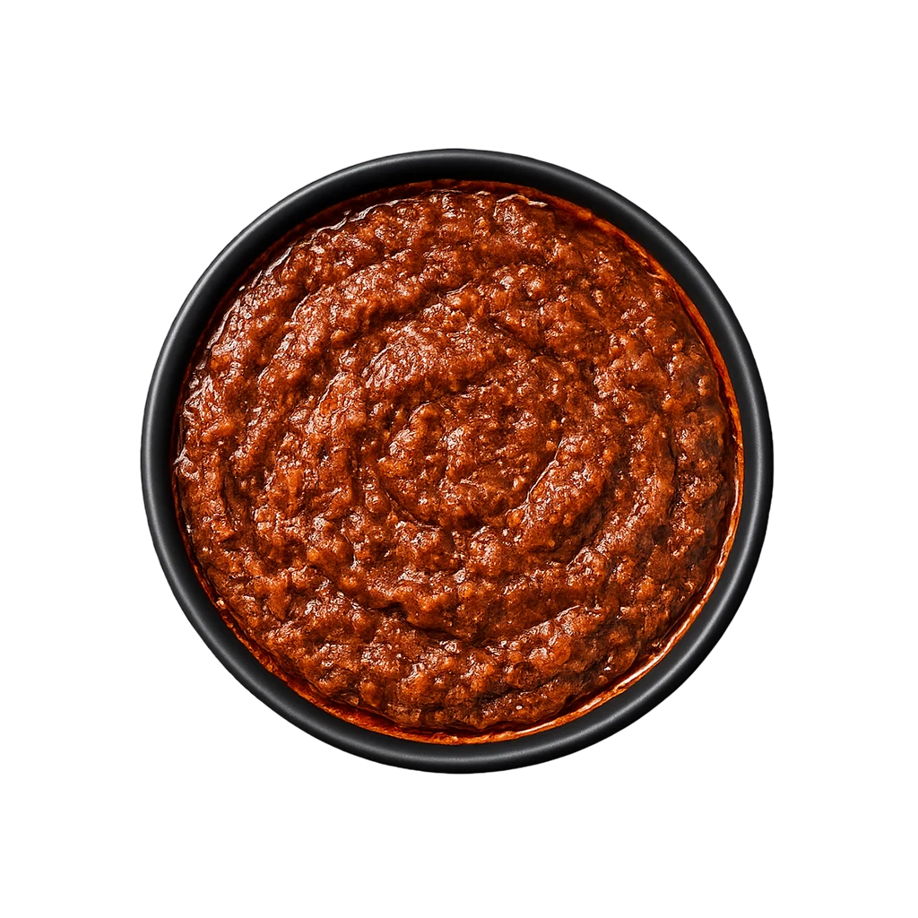 A professional 90-degree top-down flat lay of Pot and Ladle brand Andhra Nellore Biryani Paste. The concentrated masala is a deep, dark reddish-brown with a thick, textured consistency. Visible flecks of crushed spices, peppercorns, and a glossy oil sheen indicate a slow-roasted base. Served in a small, minimal black china bowl on a seamless white studio background.