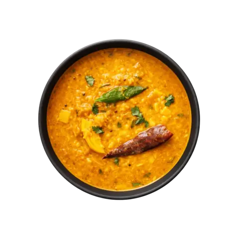 A professional 90-degree top-down shot of Pot and Ladle brand ready-to-eat Andhra Tomato Pappu. The vibrant yellow dal is slow-cooked with chunky red tomatoes and finished with a glossy tempering of mustard seeds, dried red chilies, and fresh curry leaves. Served in a minimalist black bowl on a seamless, pure white studio background.