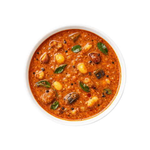 A professional 90-degree top-down flat lay of Pot and Ladle brand ready-to-eat Chettinad Kara Kuzhambu. The deep mahogany-colored tamarind gravy is rich and spicy, featuring whole pearl onions (shallots), garlic cloves, and drumsticks. The surface has a glossy sheen from the traditional gingelly oil tempering with mustard seeds and curry leaves, served in a minimal white bowl on a seamless white background.