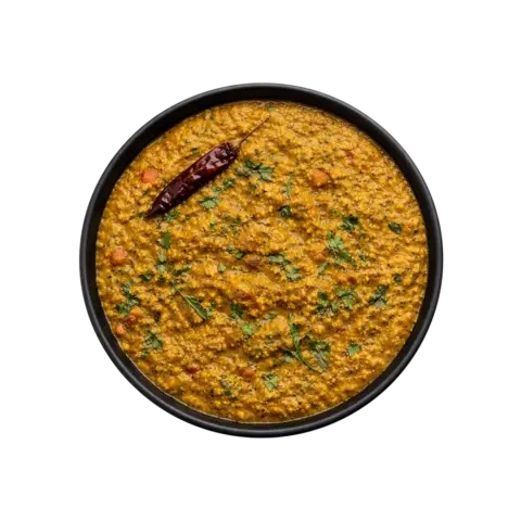 A professional 90-degree flat lay of Pot and Ladle brand ready-to-eat Gongura Pappu. The dish features creamy yellow lentils slow-cooked with tangy, finely chopped green roselle leaves (gongura) and finished with a tempering of golden garlic cloves, mustard seeds, and dried red chilies. Centered in a plain black bowl on a seamless, pure white studio background.