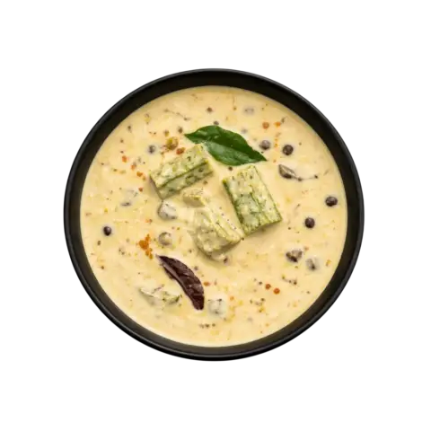 A professional 90-degree top-down flat lay of Pot and Ladle brand ready-to-eat Vendakkai Mor Kuzhambu. The dish is a creamy, light-yellow yogurt-based gravy featuring sautéed pieces of green okra (lady’s finger). The surface is garnished with a fresh tempering of mustard seeds, dried red chilies, and vibrant green curry leaves, served in a minimal black bowl on a seamless black background.