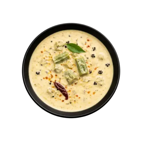 A professional 90-degree top-down flat lay of Pot and Ladle brand ready-to-eat Vendakkai Mor Kuzhambu. The dish is a creamy, light-yellow yogurt-based gravy featuring sautéed pieces of green okra (lady’s finger). The surface is garnished with a fresh tempering of mustard seeds, dried red chilies, and vibrant green curry leaves, served in a minimal black bowl on a seamless white background.